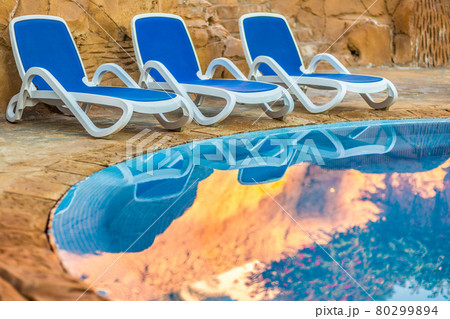 Three sunloungers reflected in blue water of the swimming pool Three sunloungers reflected in blue water of the swimming pool 80299894