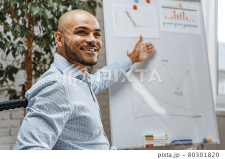 Young african american disabled man in a wheelchair makes presentation at office on whiteboard 80301820