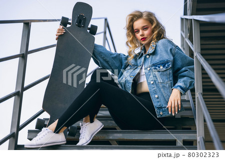 Beautiful adorable young girl in retro 90s fashion style, outfits posing on stairs, outdoors. Concept of eras comparison, beauty, fashion and youth. 80302323