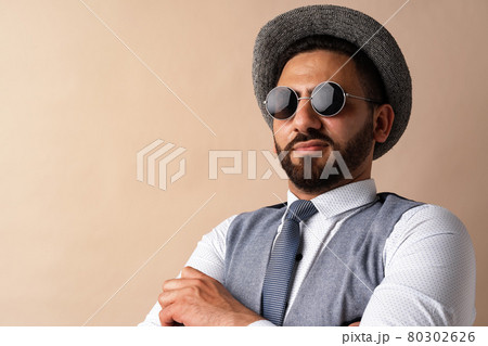 Cool egyptian man in hat and sunglasses posing against beige background 80302626