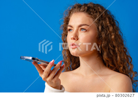 Young curly woman talking on the phone against blue background 80302627