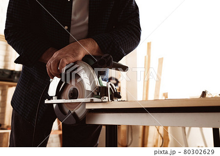 Carpenter hands cutting wood with electrical saw 80302629