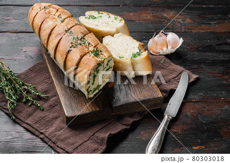 Sliced grilled bread with garlic and herbs, on old dark wooden table background Sliced grilled bread with garlic and herbs, on old dark wooden table background 80303018