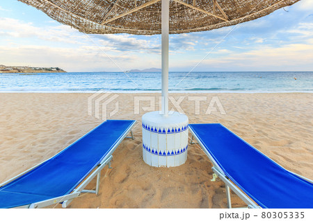Umbrella and two empty deckchairs on the shore sand beach Umbrella and two empty deckchairs on the shore sand beach 80305335