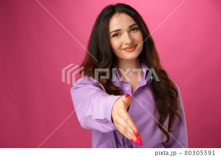 Young brunette woman giving hand for handshake against pink background 80305591