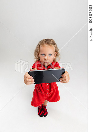 Showing device screen. One little screaming preschool girl holding smartphone isolated over white studio background. Showing device screen. One little screaming preschool girl holding smartphone isolated over white studio background. 80307683