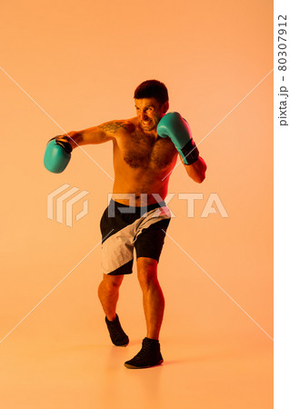 Portrait of Caucasian man, professional boxer in sportwear in action and motion on studio background in yellow neon light. Concept of sport, activity, movement, wellbeing. Portrait of Caucasian man, professional boxer in sportwear in action and motion on studio background in yellow neon light. Concept of sport, activity, movement, wellbeing. 80307912