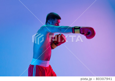 One man, professional boxer in sportwear boxing on studio background in gradient neon light. Concept of sport, activity, movement, wellbeing. One man, professional boxer in sportwear boxing on studio background in gradient neon light. Concept of sport, activity, movement, wellbeing. 80307941