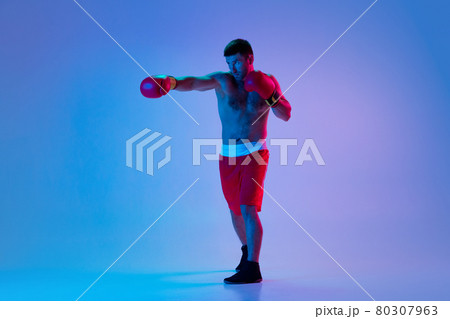 Caucasian man, professional boxer in sportwear boxing on studio background in gradient neon light. Concept of sport, activity, movement, wellbeing. Caucasian man, professional boxer in sportwear boxing on studio background in gradient neon light. Concept of sport, activity, movement, wellbeing. 80307963