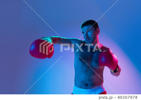 Portrait of Caucasian man, professional boxer in sportwear boxing on studio background in gradient neon light. Concept of sport, activity, movement, wellbeing. Portrait of Caucasian man, professional boxer in sportwear boxing on studio background in gradient neon light. Concept of sport, activity, movement, wellbeing. 80307978