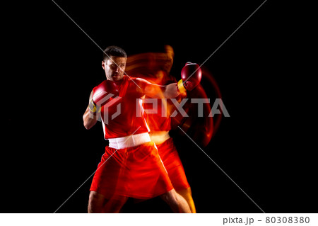 Young professional boxer in red shorts training, exercising over black background in mixed lights Young professional boxer in red shorts training, exercising over black background in mixed lights 80308380