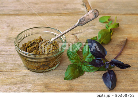 Basil pesto in glass bowl with metal spoon and green purple leaves on wooden table background above 80308755
