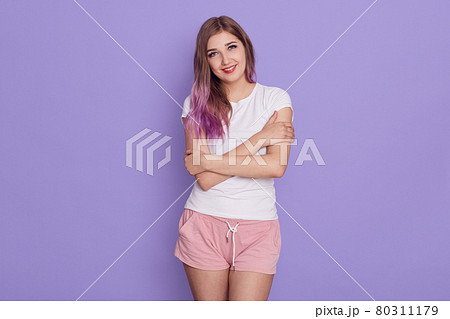 Portrait of female of young age wearing casual clothing standing and hugging herself, looking at camera with smile and love, isolated over lilac background. 80311179