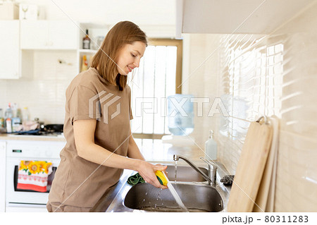woman in home t shirt washing plates with sponge in domestic kitchen. Lifestyle concept. 80311283