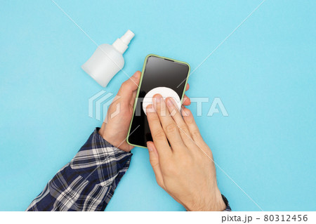 A man in a shirt disinfects his phone and wipes it with a cotton pad treated with an antiseptic. Coronavirus protection. A man in a shirt disinfects his phone and wipes it with a cotton pad treated with an antiseptic. Coronavirus protection. 80312456