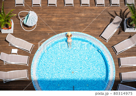Young alone beautiful sports woman in bikini and hat is swimming in jacuzzi on wooden terrace. Aerial drone view from above. Tropical summer luxury hotel 80314975