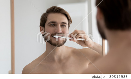 Positive handsome well built guy brushing teeth in bathroom 80315983