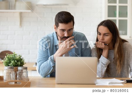 Serious concerned couple sit indoor looking at laptop read news Serious concerned couple sit indoor looking at laptop read news 80316001
