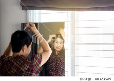 Elderly Asian woman plucking gray hair with tweezers on mirror,Selective focus 80323589