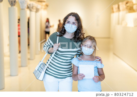 Little daughter and mother in protective masks inspect the exhibits in museum 80324712
