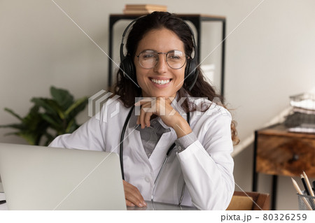 Smiling female doctor in headphones work online on laptop 80326259