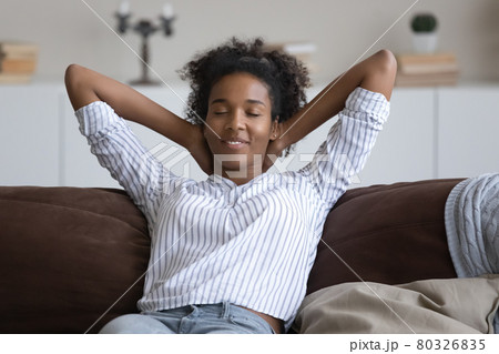 Peaceful smiling African American woman resting leaning back on couch 80326835