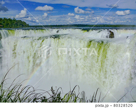 アルゼンチン・ブラジル国境エリアのイグアスの滝にて虹のかかった悪魔の喉笛と青空 80328520