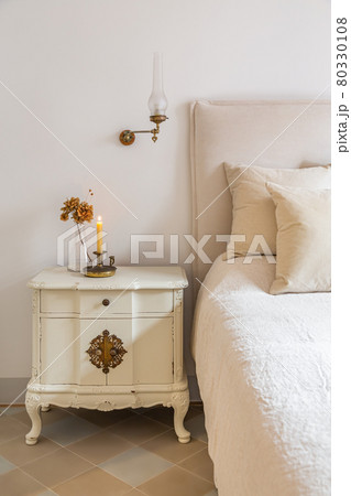 Classic bedroom with wooden bedside table with burning candle and flowers near comfortable bed. Interior of cozy home in retro style. Classic bedroom with wooden bedside table with burning candle and flowers near comfortable bed. Interior of cozy home in retro style. 80330108