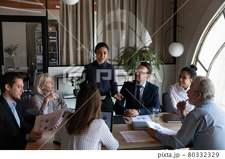 Female Indian business leader talking to diverse team, discussing reports Female Indian business leader talking to diverse team, discussing reports 80332329