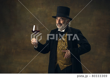 Portrait of elderly gray-haired man, gentleman, aristocrat or actor tasting wine isolated on dark vintage background. Retro style, comparison of eras concept. 80333369