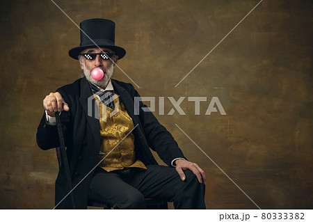 Cute senior smiling man, gentleman, aristocrat or actor watching movie isolated on dark vintage background. Retro style, comparison of eras concept. Cute senior smiling man, gentleman, aristocrat or actor watching movie isolated on dark vintage background. Retro style, comparison of eras concept. 80333382