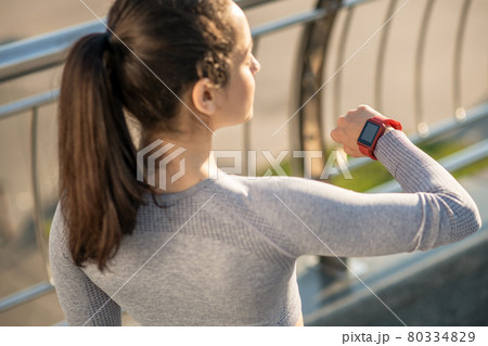 Waist up picture of a long-haired girl looking at her smartwatch 80334829