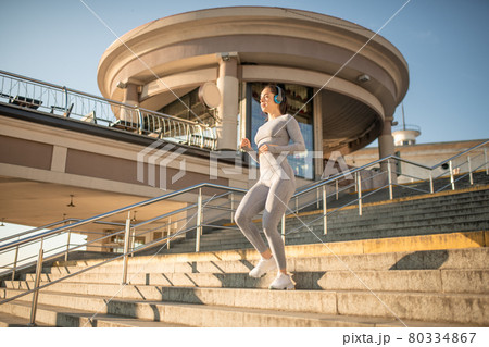 Fit girl in grey sportswear having cardio warm up on the stairs 80334867