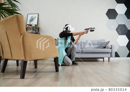Woman with virtual reality headset and blaster is playing game. 80335014
