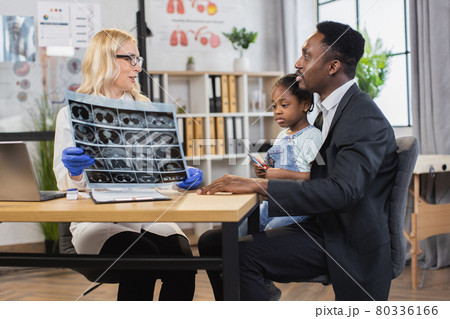 Woman doctor holding x-ray scan, talking with black-skinned father with cute mixed race daughter 80336166