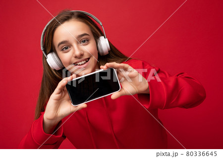 Closeup portrait of beautiful brunette girl wearing red hoodie isolated on red background holding 80336645