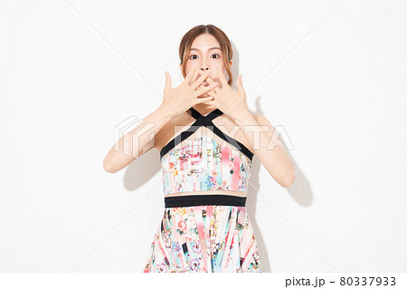 白い壁の前に立って、驚いたジェスチャーをする、ワンピースを着た若い女性 80337933