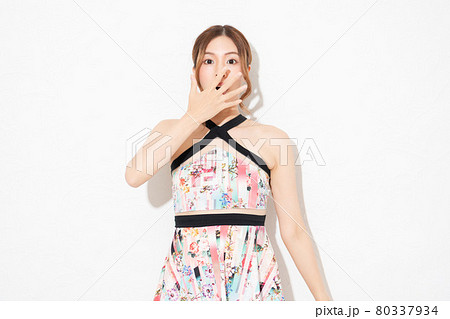 白い壁の前に立って、驚いたジェスチャーをする、ワンピースを着た若い女性 80337934