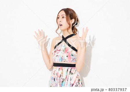 白い壁の前に立って、驚いたジェスチャーをする、ワンピースを着た若い女性 80337937