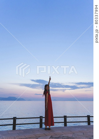 夕暮れの海にいる赤いワンピースの女性 80337994