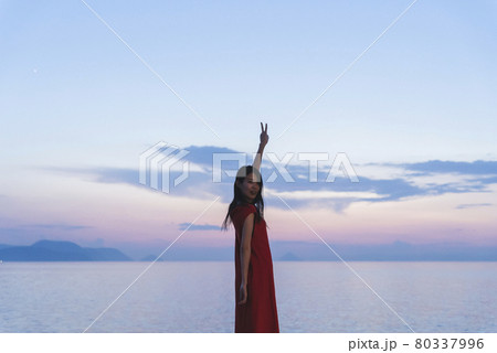 夕暮れの海にいる赤いワンピースの女性 80337996