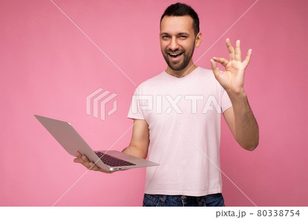 Handsome happy and funny brunet man holding laptop computer and showing gesture okay looking at 80338754