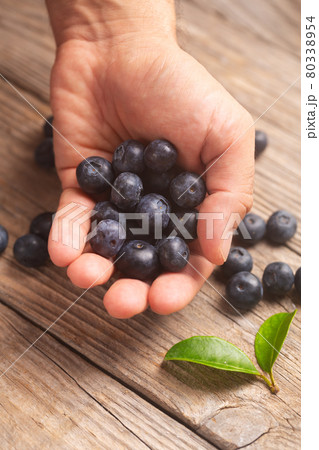 Male hand holding blueberries on wooden background Male hand holding blueberries on wooden background 80338954