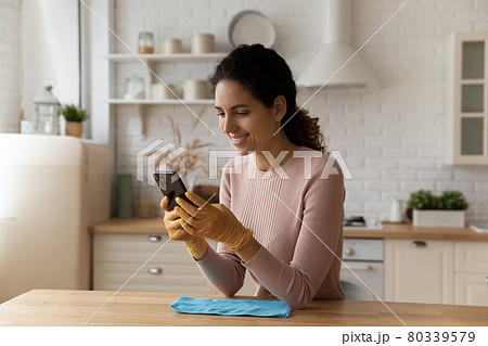 Distracted from cleaning young woman sending message on smartphone. 80339579