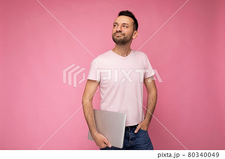 Handsome happy young unshaven man holding laptop computer looking up in t-shirt on isolated pink 80340049