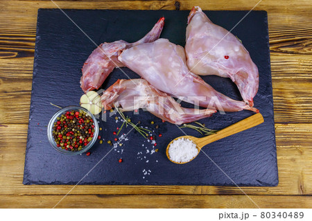 Raw rabbit legs with spices on a black slate cutting board on wooden table. Top view Raw rabbit legs with spices on a black slate cutting board on wooden table. Top view 80340489