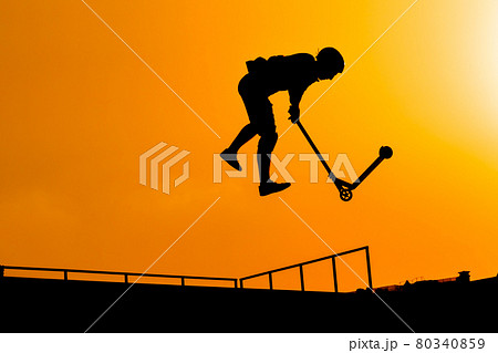 Teenager silhouette showing high jump tricks on scooter against sunset sky Teenager silhouette showing high jump tricks on scooter against sunset sky 80340859