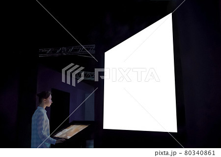 Woman using kiosk and looking at large blank white screen in dark room Woman using kiosk and looking at large blank white screen in dark room 80340861