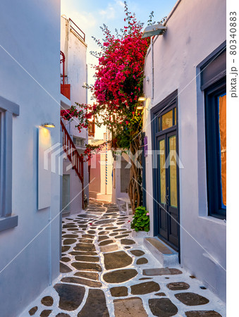 Beautiful traditional narrow cobbled alleys of Greek island towns. Whitewashed houses, shops, morning summer sunshine, bougainvillea, Mykonos, Greece. 80340883