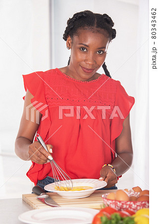 Afro american woman smiling at the camera while whisking eggs: Cooking concept 80343462
